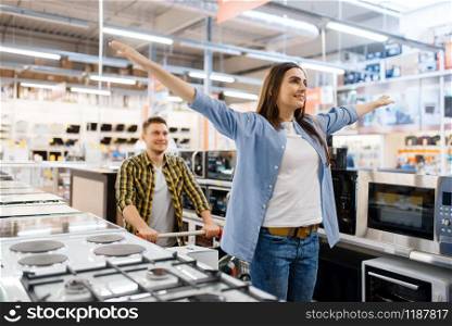 Happy family couple with cart in electronics store. Man and woman buying home electrical appliances in market. Happy family couple in electronics store