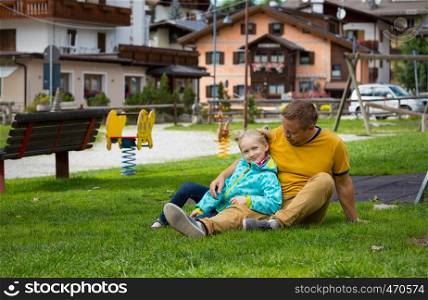 happy family. dad with daughter sitting on a lawn in a park in Canazei, Italy