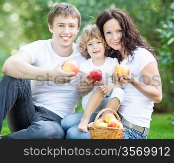 Happy family eating apples outdoors in spring park. Healthy lifestyle concept