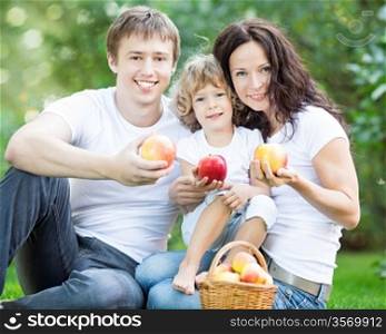 Happy family eating apples outdoors in spring park. Healthy lifestyle concept