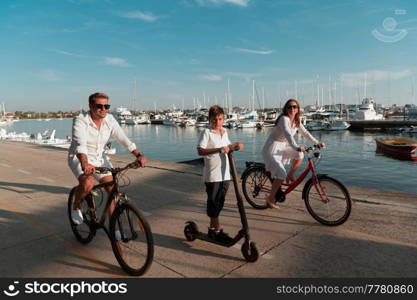 Happy family enjoying a beautiful morning by the sea together, parents riding a bike and their son riding an electric scooter. Selective focus. High-quality photo. Happy family enjoying a beautiful morning by the sea together, parents riding a bike and their son riding an electric scooter. Selective focus