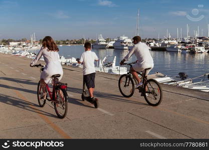 Happy family enjoying a beautiful morning by the sea together, parents riding a bike and their son riding an electric scooter. Selective focus. High-quality photo. Happy family enjoying a beautiful morning by the sea together, parents riding a bike and their son riding an electric scooter. Selective focus