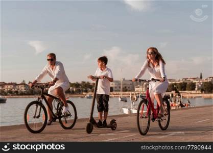 Happy family enjoying a beautiful morning by the sea together, parents riding a bike and their son riding an electric scooter. Selective focus. High-quality photo. Happy family enjoying a beautiful morning by the sea together, parents riding a bike and their son riding an electric scooter. Selective focus