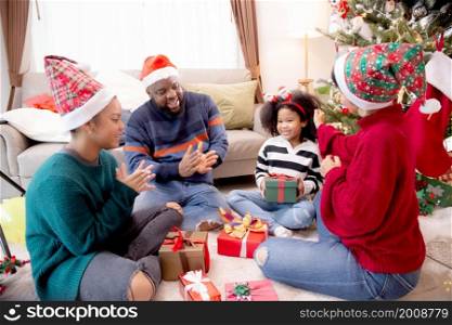 Happy family father and mother giving gift box with daughter on celebration in Christmas day at home, xmas with parent surprising children with enjoyment at house, thanksgiving eve, Merry Christmas.