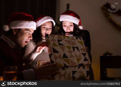 happy family, father mother daughter help to open gift present box together at christmas day night in dining room that decorated with christmas tree for christmas festival day