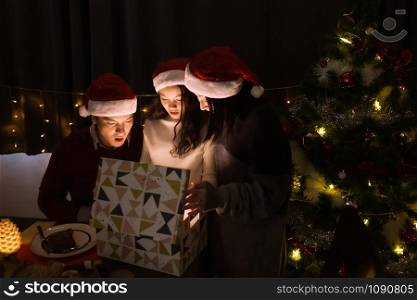 happy family, father mother daughter help to open gift present box together at christmas day night in dining room that decorated with christmas tree for christmas festival day