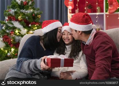 happy family, father mother give gift present and kiss daughter, they celebrate together at christmas day night in living room that decorated with christmas tree for christmas festival day