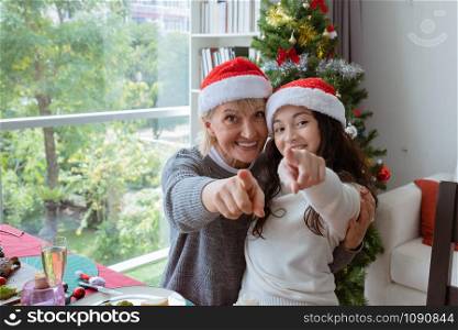 happy family, grandmother smile and hug daughter little girl and point at camera together in christmas room that decorated with christmas tree christmas festival day, happy family holiday concep