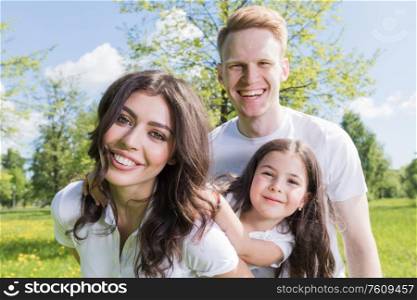 Happy family having fun outdoors in spring park against natural green meadow and trees background. Happy family in spring park