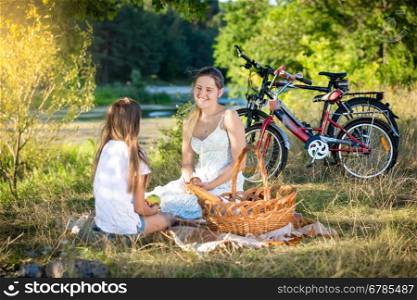 Happy family having picnic by the river. Smiling mother and daughter looking at each other