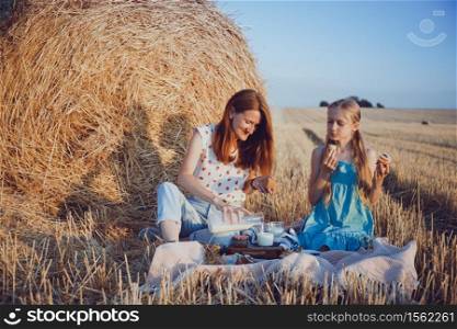 happy family in a wheat field. mother and daughter on a picnic in a field near Round Bales at sunset time.