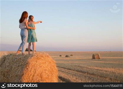 happy family in a wheat field. mother and daughter posing on a Round Bales at sunset time.