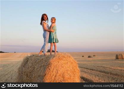 happy family in a wheat field. mother and daughter posing on a Round Bales at sunset time.