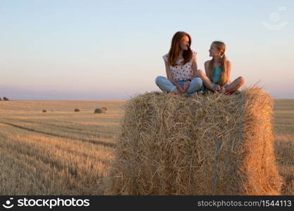 happy family in a wheat field. mother and daughter posing on a Round Bales at sunset time.