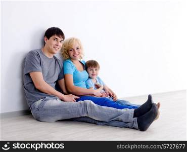 Happy family in casuals with little son sitting on the floor in empty room - indoors