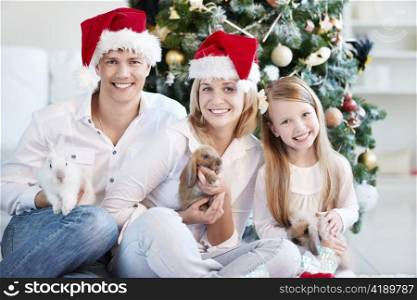 Happy family in Christmas caps with the rabbits on the background of trees