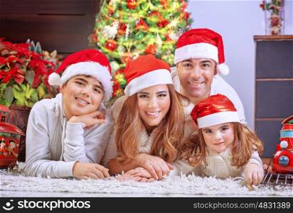 Happy family in Christmas eve, cheerful parents with two cute kids lying down on the floor near beautiful decorated Xmas tree