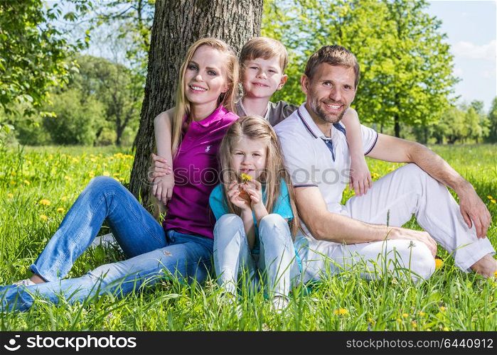 Happy family in city par. Happy family with man, woman and two children leaning on tree in city park