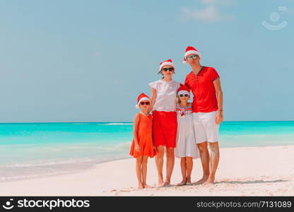 Happy family in Santa hats on a tropical beach celebrating Christmas vacation. Happy family with two kids in Santa Hat on summer vacation