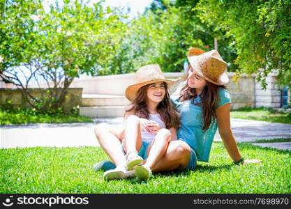 Happy family in the garden, beautiful mother with her little cute daughter sitting on fresh green grass on backyard, with pleasure spending time together