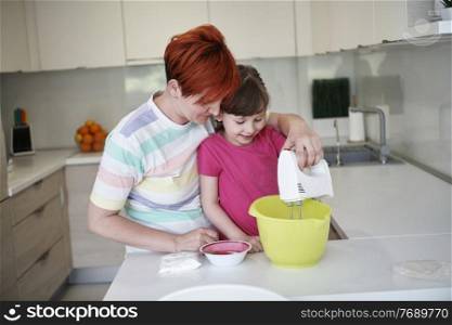 Happy family in the kitchen playing games and learning to cooking while staying at home during coronavirus covid-19 pandemic isolation. Mother and child daughter preparing the cake and cookies.
