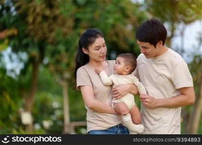 happy family in the park. father and mother talking and playing with infant baby.