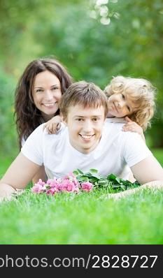 Happy family lying on grass in spring park against blurred green background