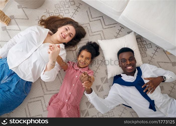 Happy family lying on the floor in living room. Mother, father and their daughter poses at home together, good relationship. Happy family lying on the floor in living room