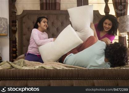 Happy family members playing with pillows together on bed