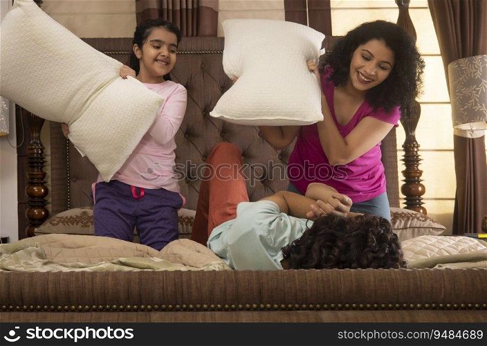 Happy family members playing with pillows together on bed