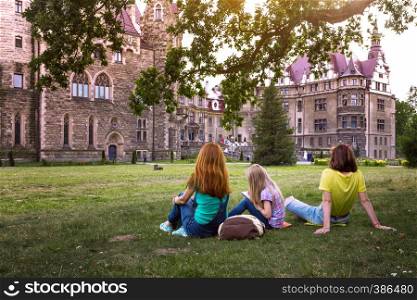 Happy family - mom and two daughters are sitting in a meadow Beautiful castle on the background