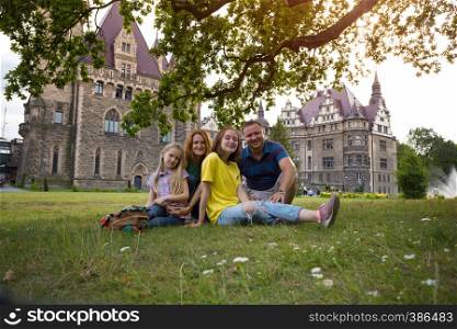 Happy family - mom, dad and two daughters are sitting in a meadow Beautiful castle on the background