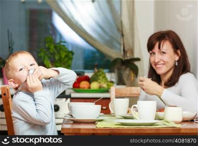 Happy family. Mother and blond son boy kid child eating corn flakes and bread breakfast morning meal together at the table. Home.