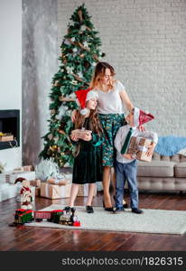 Happy family, mother and children unpack gifts under the Christmas tree sitting by the fireplace, Christmas morning. Merry Christmas.. Happy family, mother and children unpack gifts under the Christmas tree sitting by the fireplace, Christmas morning.