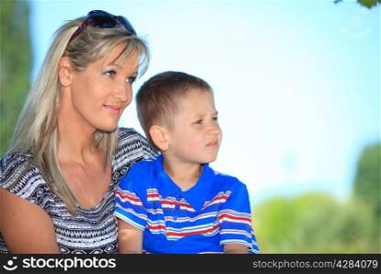 Happy family mother and her child boy on bench in park enjoy the summer