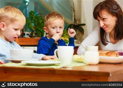 Happy family. Mother and sons boys kids children eating corn flakes and bread breakfast morning meal together at the table. Home.
