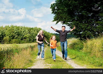 Happy family (mother, father and kid) having a walk in the nature playing tag