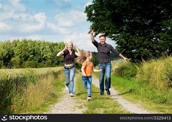 Happy family (mother, father and kid) having a walk in the nature playing tag
