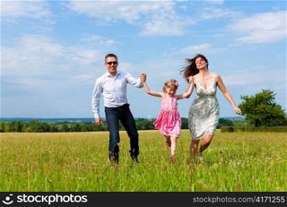 Happy family - mother, father, child - running over a green meadow in summer