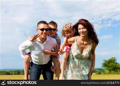 Happy family - mother, father, children - standing on a meadow in summer piggyback the kids