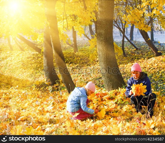 Happy family (mother with daughter) in golden evening maple autumn park and sunshine behind the tree foliage