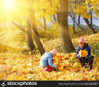 Happy family (mother with daughter) in golden evening maple autumn park and sunshine behind the tree foliage