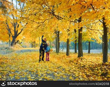 Happy family (mother with daughter) walking in golden maple autumn park