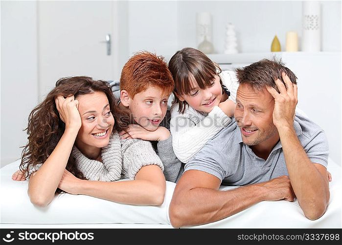 Happy family of 4 people laying on a sofa at home