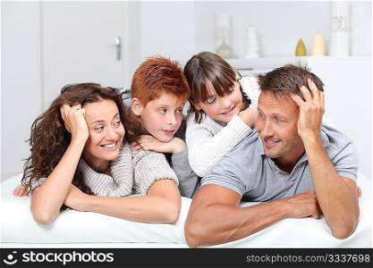 Happy family of 4 people laying on a sofa at home
