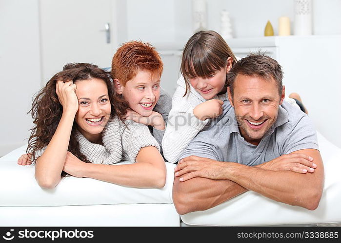 Happy family of 4 people laying on a sofa at home