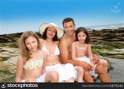 Happy family of 4 people sitting at the beach