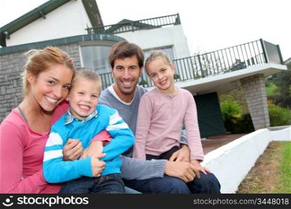Happy family of 4 people sitting in front of new home