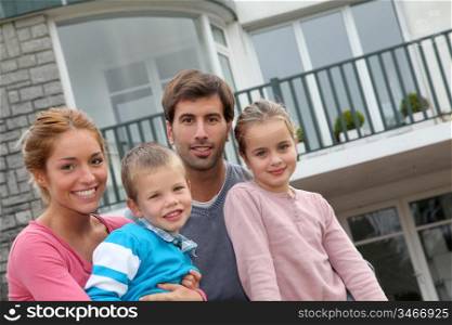 Happy family of 4 people sitting in front of new home
