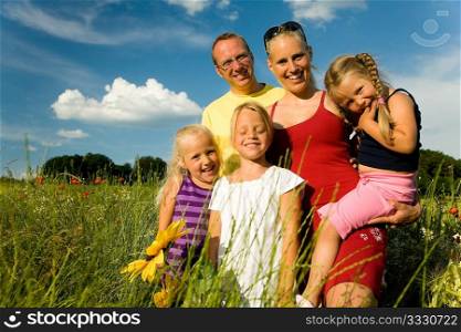 Happy family of five standing in the grass with and flowers together - metaphor for love